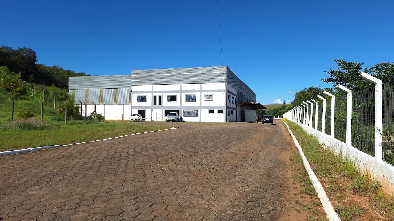 Galpão da operação em Pouso Alegre visto do pátio de acesso, com prédio administrativo à frente e área de docas à direita.